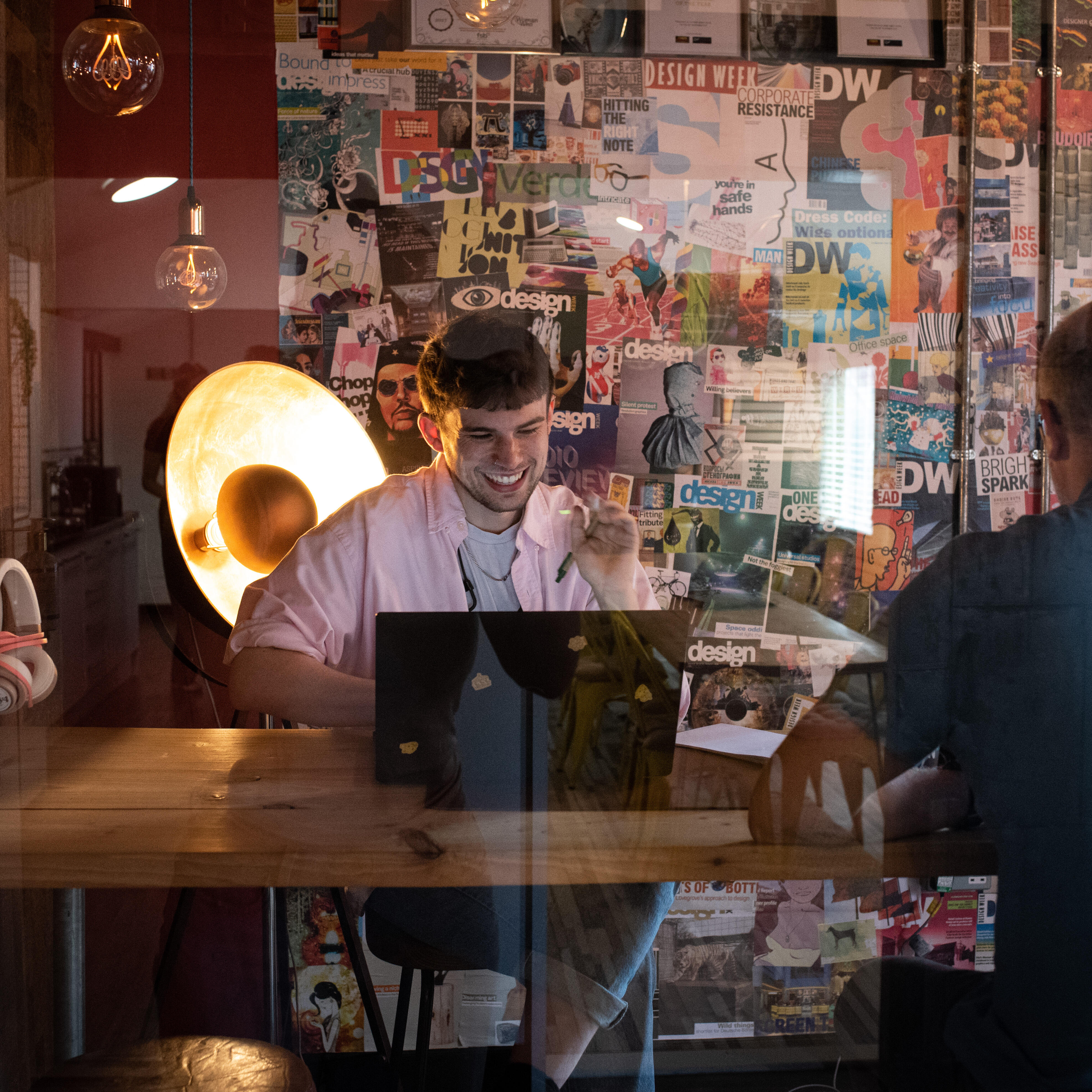 Zwei Personen sitzen an einem Holztisch in einem kreativ gestalteten Büro mit Design-Postern an der Wand und arbeiten an Laptops.