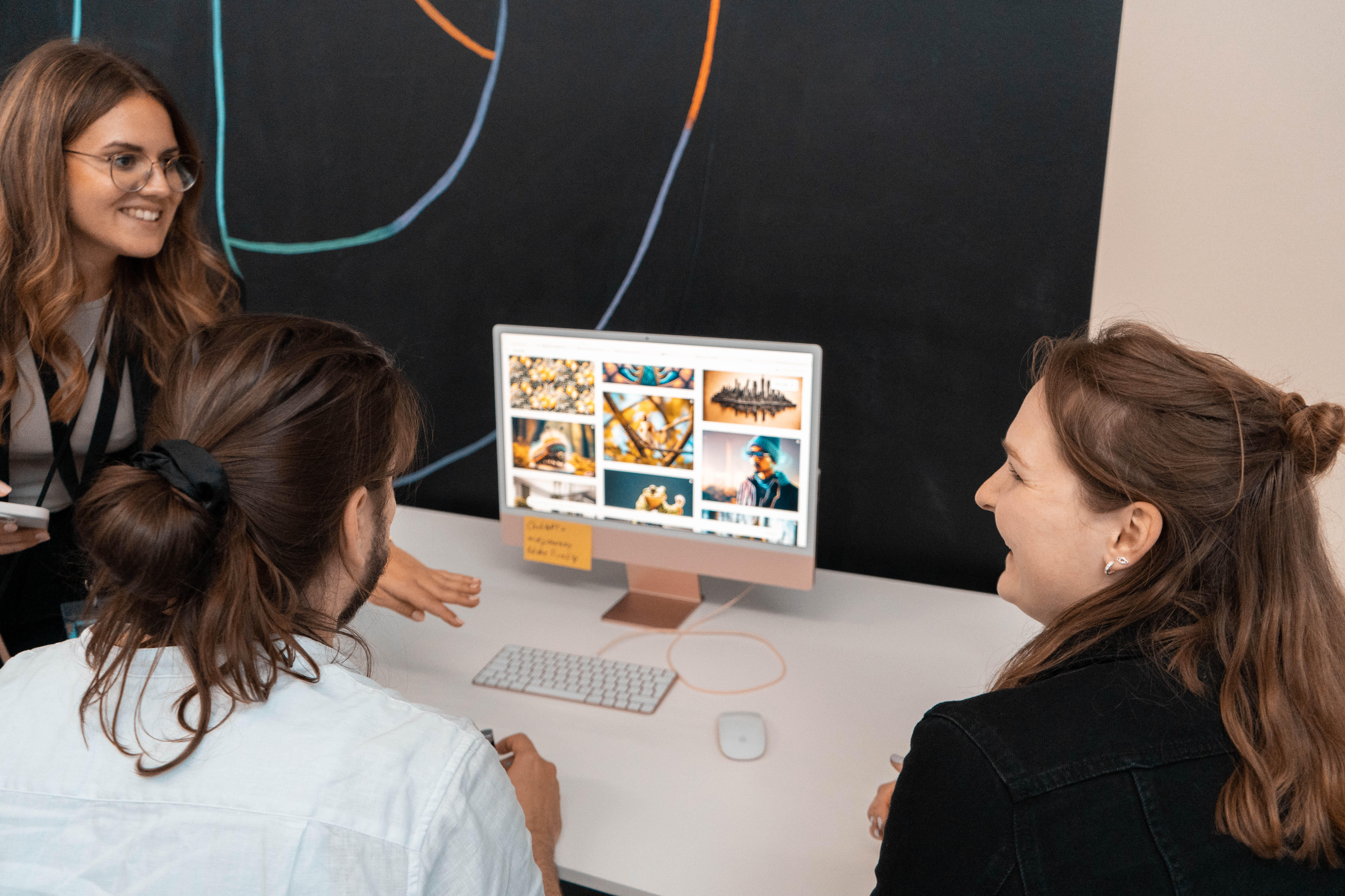 Drei Personen sitzen an einem Schreibtisch und betrachten gemeinsam einen Computerbildschirm, auf dem verschiedene Bilder und Grafiken angezeigt werden.