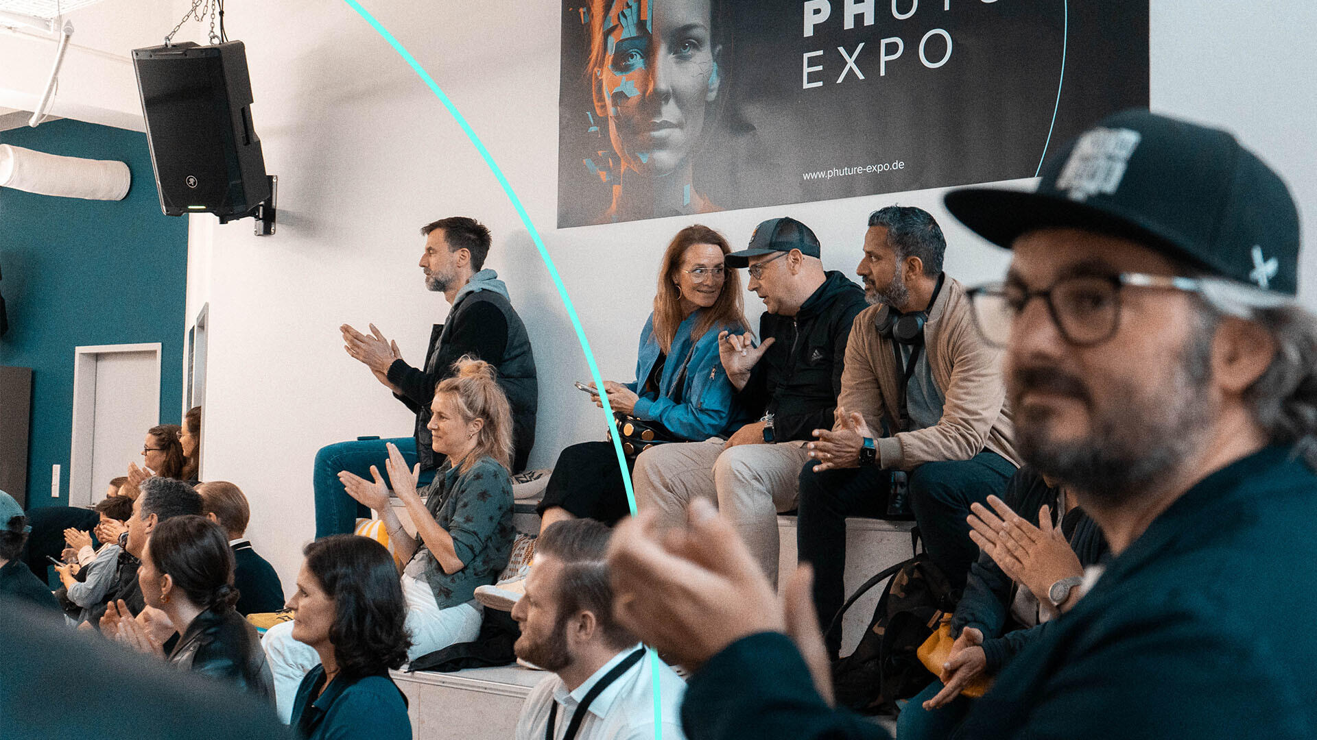 Menschen sitzen und applaudieren bei einer Veranstaltung in einem modernen Raum, im Hintergrund hängt ein Banner mit der Aufschrift "PHOTO EXPO".