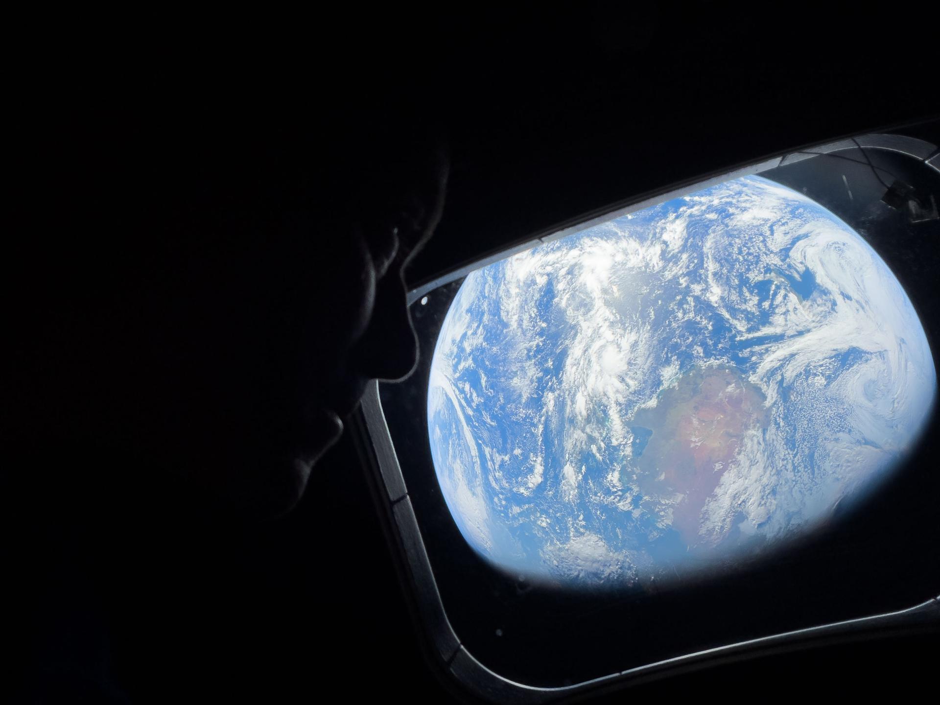 art002e008486 (April 4, 2026) - NASA astronaut and Artemis II Commander Reid Wiseman peers out of one of the Orion spacecraft's main cabin windows, looking back at Earth, as the crew travels towards the Moon.